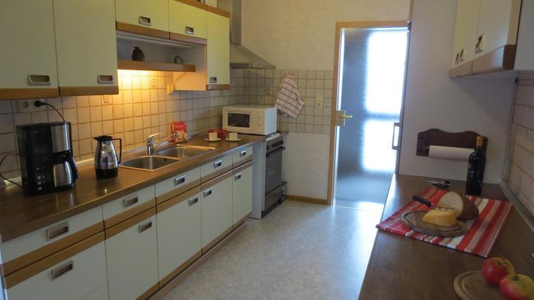 Eine moderne Küche mit hellen Schränken und einer Holzarbeitsplatte. Auf der Arbeitsfläche stehen Äpfel und eine Platte mit Brot.