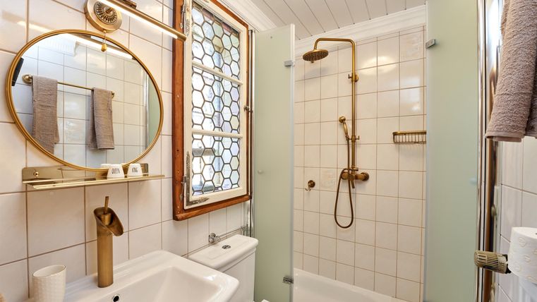 Ein modernes Badezimmer mit einer Dusche und einer weißen Badewanne. Es verfügt über elegante goldene Armaturen und ein großes, rundes Spiegel.