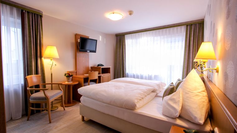 Ein helles Hotelzimmer mit einem Doppelbett und einer angenehmen Atmosphäre. Der Raum ist mit einem Fernseher, einem Schreibtisch und bequemen Stühlen ausgestattet.