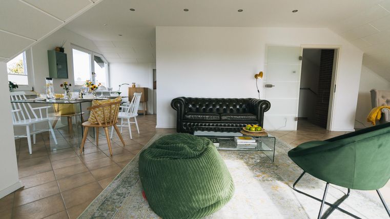 Ein modernes Wohnzimmer mit einem eleganten schwarzen Sofa und einem runden Sessel. Der Raum ist hell und freundlich, mit einem Esstisch und bunten Stühlen im Hintergrund.