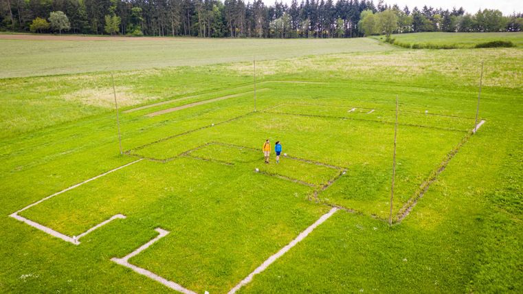 Aerial view of two people on a field with marked ground plans of a Roman villa.