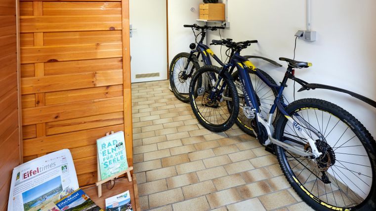 Ein Flur mit zwei modernen Mountainbikes und einem Holzregal. An der Wand hängen Informationsmaterialien über die Region.