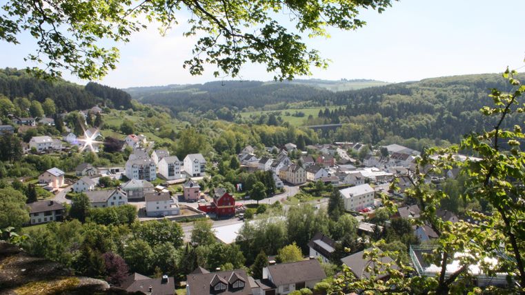 Eine schöne Aussicht auf ein Dorf umgeben von grünen Hügeln. Die Häuser sind verstreut zwischen Bäumen und Wiesen.