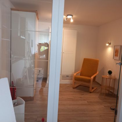 A bright room with modern design. An orange desk chair stands next to a small table and a decorative accessory.