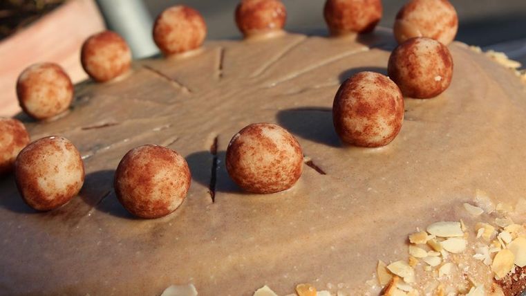 Eine leckere Torte mit einer glatten Oberfläche und dekorativen Schokoladenkugeln. Mandeln umgeben die Basis der Torte.