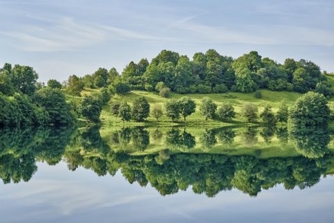 Een rustige meer met spiegelend water en weelderig groen eromheen. De bomen en heuvels weerspiegelen prachtig in het water.