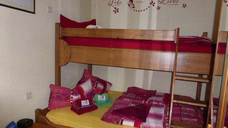 Ein gemütliches Schlafzimmer mit einem Hochbett und einem Einzelbett. Die Wände sind mit einem liebevollen Spruch dekoriert.