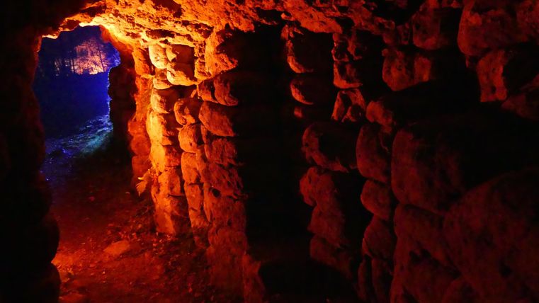 Ein geheimnisvoller Tunnel mit beleuchteten Felswänden in warmen Farbtönen. Der Hintergrund ist dunkel und ist von blauen Lichtquellen durchzogen.