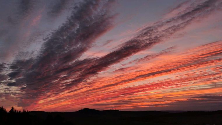 Ein atemberaubender Sonnenuntergang mit leuchtenden Farben am Himmel. Die Wolken ziehen in verschiedenen Mustern über die Landschaft.