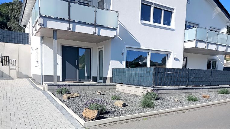 Ein modernes Haus mit einem hellen Außenbereich. Der Eingangsbereich ist sauber gestaltet, umgeben von kleinen Pflanzen und Steinen.