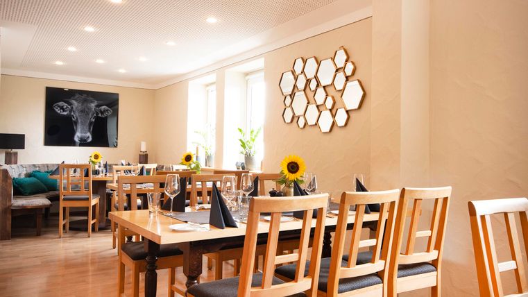 Ein einladendes Restaurant mit Holzstühlen und Tischen. An der Wand hängen dekorative Spiegel und eine Kuhgrafik.