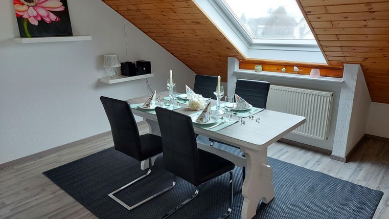 Ein modern gestalteter Essbereich mit einem Tisch und schwarzen Stühlen. Das Dachfenster lässt viel Licht herein und eine Blumenmalerei schmückt die Wand.