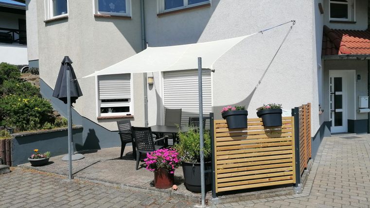Ein gemütlicher Außenbereich mit einem weißen Sonnensegel und Terrassenmöbeln. Blumen in Töpfen ergänzen die einladende Atmosphäre.