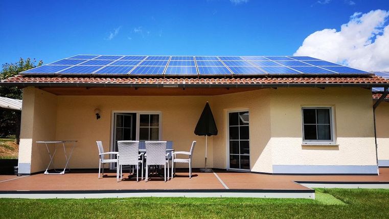Ein modernes Haus mit Solarpanelen auf dem Dach und einem gemütlichen Außenbereich. Der grüne Rasen und die blauen Himmel sorgen für eine angenehme Atmosphäre.