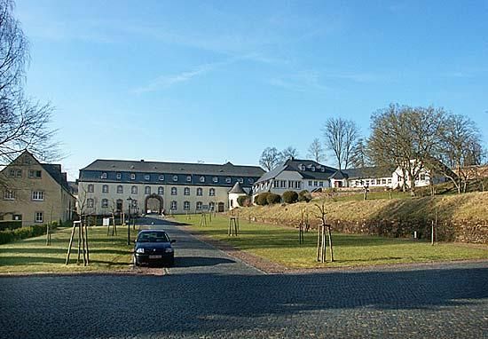 Ein Portal zu einem historischen Gebäude mit einer gepflegten Grünanlage. Der Himmel ist klar und es herrscht eine ruhige Atmosphäre.