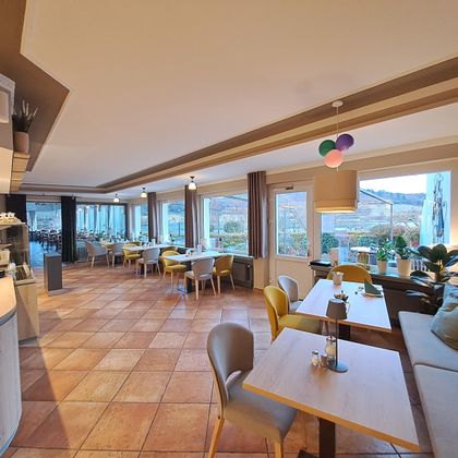 Ein modernes Restaurant mit hellen Fenstern und bunten Stühlen. Der Raum ist freundlich und einladend gestaltet.
