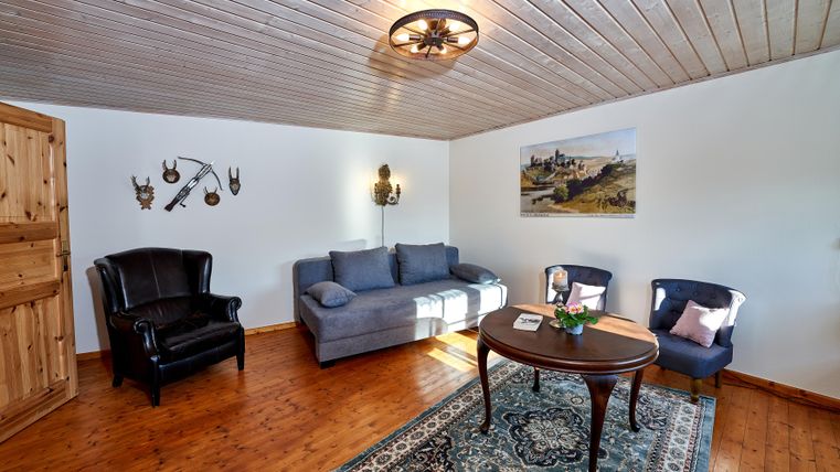 Ein gemütliches Wohnzimmer mit einem blauen Sofa und zwei dunkelblauen Stühlen. Der Holzboden und die rustikale Dekoration verleihen dem Raum eine einladende Atmosphäre.