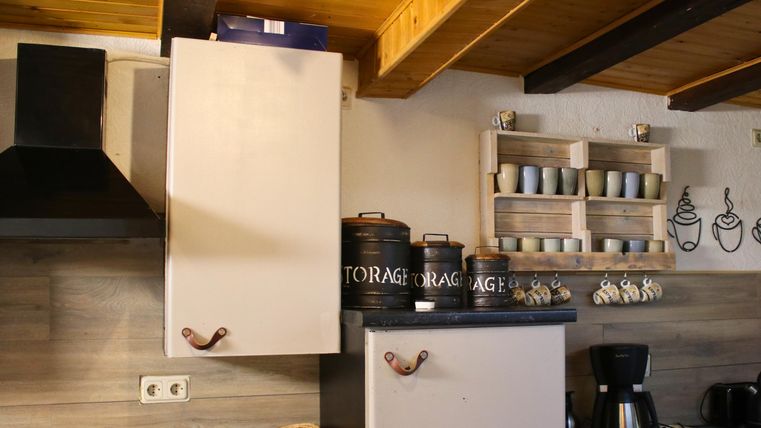 Eine gemütliche Küche mit Holzregalen und dekorativen Kaffeetassen. Auf der Arbeitsfläche stehen Küchengeräte und Behälter für die Aufbewahrung.