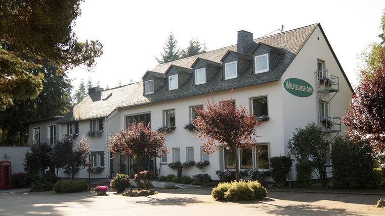 Ein gemütliches Gebäude mit einem einladenden Eingangsbereich. Umgeben von Bäumen und Blumensträuchern, strahlt es eine freundliche Atmosphäre aus.