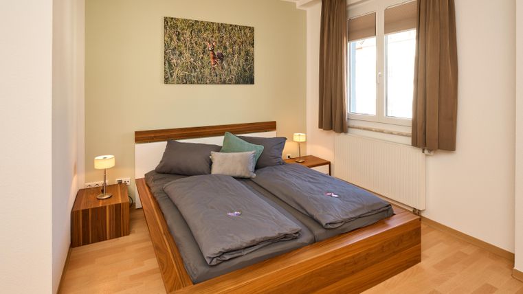 Ein gemütliches Schlafzimmer mit einem Doppelbett und modernen Ergänzungen. Zwei Nachttische mit Lampen und ein großes Fenster sorgen für ein helles Ambiente.