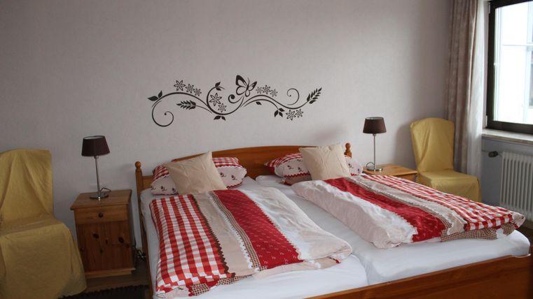 Ein gemütliches Schlafzimmer mit einem Doppelbett und bunten Bettdecken. An der Wand befindet sich eine dekorative Verzierung und neben dem Bett stehen zwei Nachttische mit Lampen.