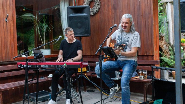 Zwei Musiker spielen in einem gemütlichen Innenhof. Einer spielt Gitarre, während der andere am Keyboard sitzt und singt.