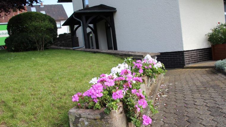 Ein gepflegter Garten mit bunten Blumen in einem Beet. Im Hintergrund ist ein Haus mit klaren Linien zu sehen.