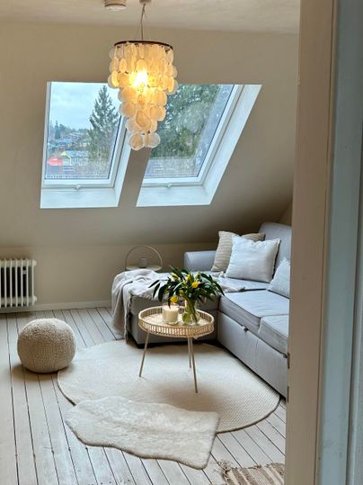 Ein heller, einladender Wohnraum mit Dachfenstern und modernem Möbel. Die Einrichtung ist gemütlich und minimalistisch gestaltet.