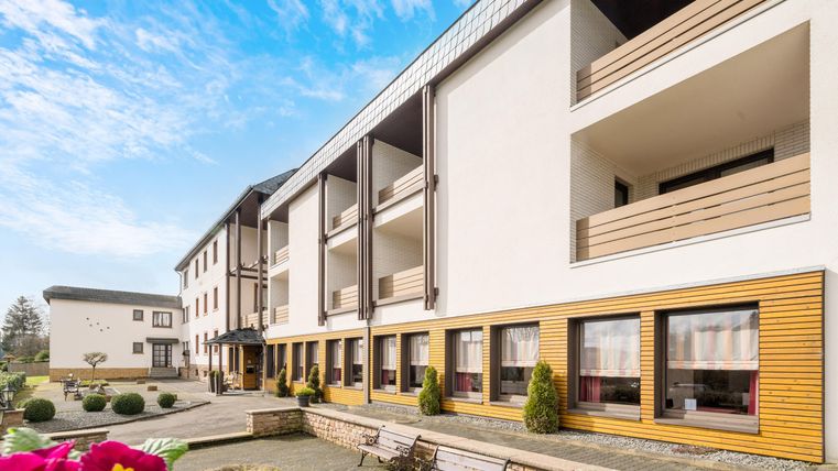 Ein modernes Gebäude mit einem klaren blauen Himmel. Der Eingangsbereich ist ansprechend gestaltet und von gepflegten Pflanzen umgeben.
