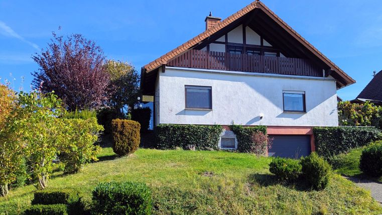 Ein schönes Haus auf einem Hügel mit einem gepflegten Garten. Die Sonne scheint und der Himmel ist blau.