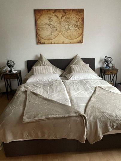 Ein gemütliches Schlafzimmer mit einem Doppelbett und modernen Nachttischen. An der Wand hängt ein antik aussehendes Kartenbild.