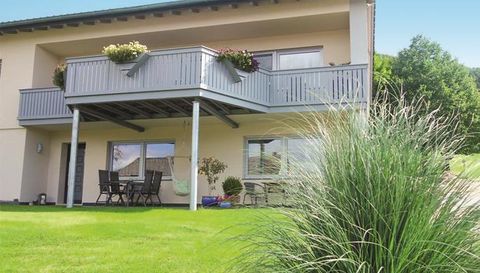 Ein modernes Haus mit einem Balkon und blühenden Pflanzen. Der gepflegte Garten und die grüne Wiese schaffen eine einladende Atmosphäre.