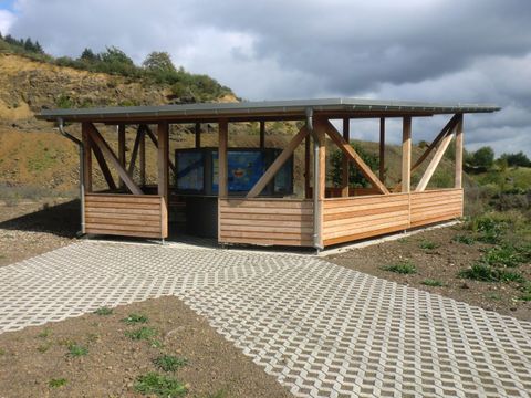 Ein modernes Holzgebäude mit großen Fenstern steht auf einem gepflasterten Weg. Im Hintergrund sind sanfte Hügel zu sehen.