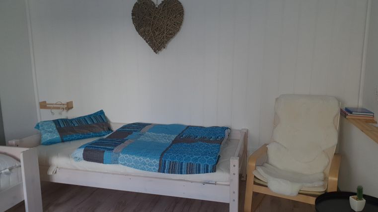 Ein gemütliches Schlafzimmer mit einem weißen Bett und einem bequemen Stuhl. An der Wand hängt ein Herz aus Rattan.