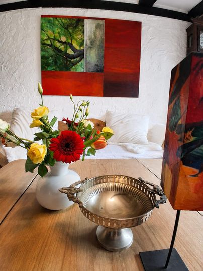 Ein eleganter Tisch mit einer silbernen Schale und einer Blumenvase voller bunter Blumen. Im Hintergrund hängt ein modernes Gemälde mit lebhaften Farben.