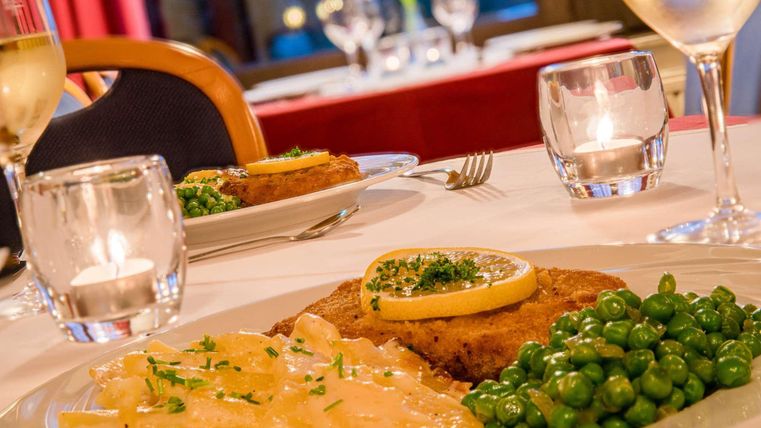 Ein schön dekorierter Tisch in einem Restaurant mit einem Gericht aus gebratenem Fisch, grünen Erbsen und Kartoffeln. Im Hintergrund sind Kerzen und Gläser zu sehen, die eine angenehme Atmosphäre schaffen.