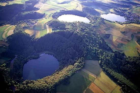 Eine Luftaufnahme von mehreren Seen, die von grünen Wäldern umgeben sind. Die Landschaft ist hügelig und agrarisch gestaltet.
