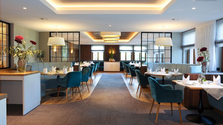 Ein elegantes Restaurant mit modernem Design und stilvollen blauen Stühlen. Der Raum ist hell beleuchtet und dekoriert mit Blumenarrangements.