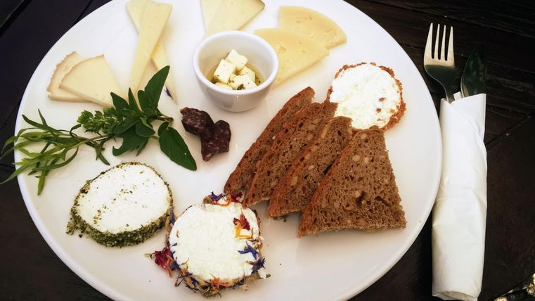 Ein Teller mit verschiedenen Käsesorten, frischem Brot und Kräutern. Dazu befindet sich eine kleine Schale mit Feta-Käse.