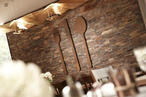 Eine stilvolle Wand mit einem Steinmuster und metallischen Messer-, Gabel- und Löffeldesigns. Der Raum wirkt einladend und modern.
