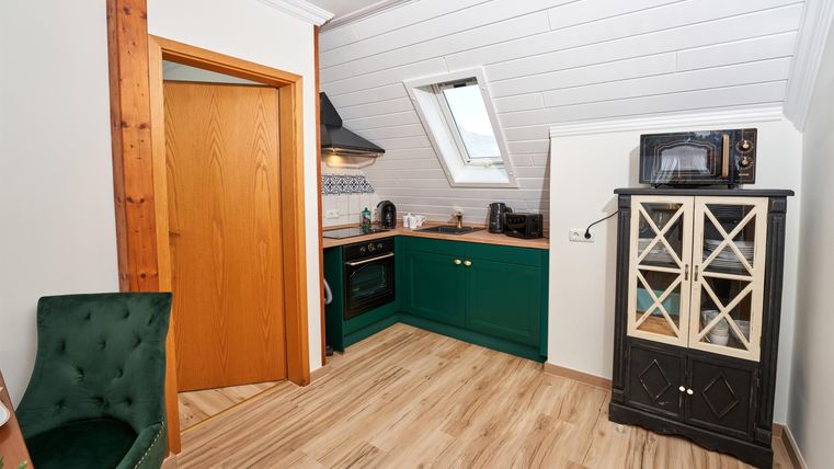 Eine moderne Küche mit grünen Schränken und hellen Holzfußböden. Es gibt ein Fenster, das natürliches Licht hereinlässt.