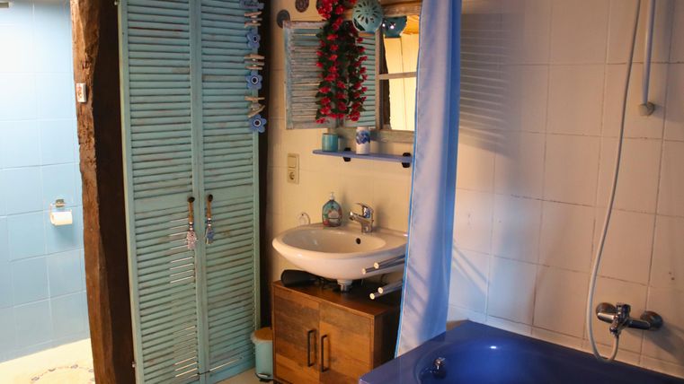 Ein lichtdurchflutetes Badezimmer mit blauen Akzenten. Es gibt eine Badewanne, ein Waschbecken und einen offenen Zugang zur Duschkabine.