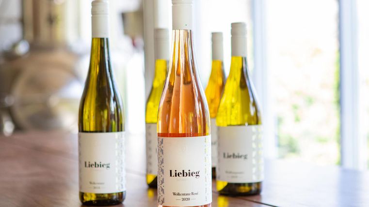 Eine ansprechende Anordnung von Weinflaschen auf einem Tisch. Im Vordergrund steht eine Flasche Roséwein, umgeben von mehreren Flaschen Weißwein.