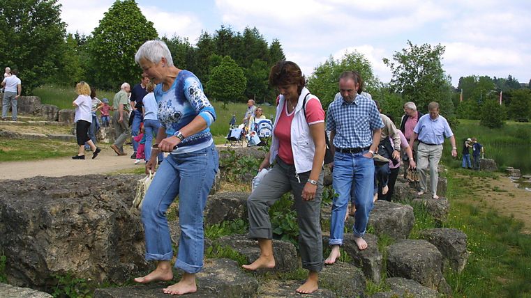 Menschen gehen barfuß über Steine auf einem Barfußpfad in Hillesheim.