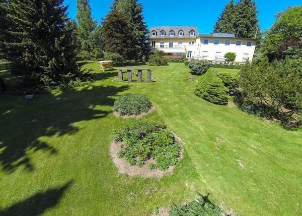 Ein weitläufiger Garten mit gepflegtem Rasen und verschiedenen Pflanzen. Im Hintergrund steht ein helles Gebäude umgeben von Bäumen.