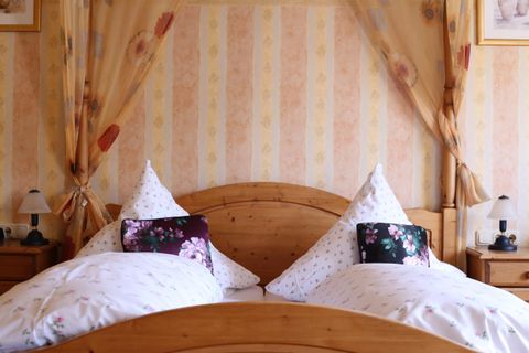 Ein gemütliches Schlafzimmer mit einem Holzbett und dekorativen Kissen. Die Wände sind in sanften Farben mit einem blumigen Muster gestaltet.