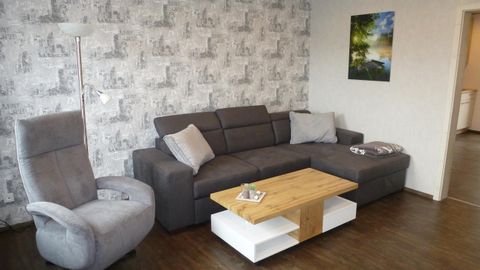 Ein modernes Wohnzimmer mit einem grauen Sofa und einem beigen Sessel. Der Holztisch in der Mitte ergänzt die gemütliche Atmosphäre.