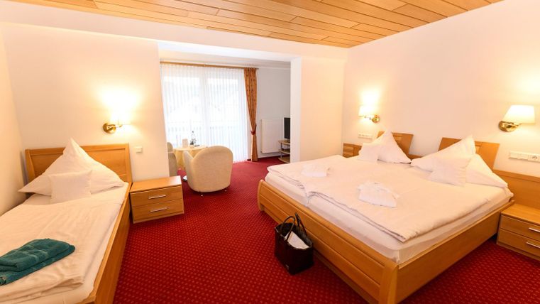 Ein gemütliches Schlafzimmer mit zwei Betten und einem Einzelbett. Der Raum hat ein warmes, einladendes Ambiente und viel Tageslicht.