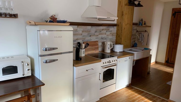 Eine moderne Küche mit weißen Möbeln und Holzfußboden. Die Ausstattung umfasst einen Kühlschrank, Herd und Spüle.