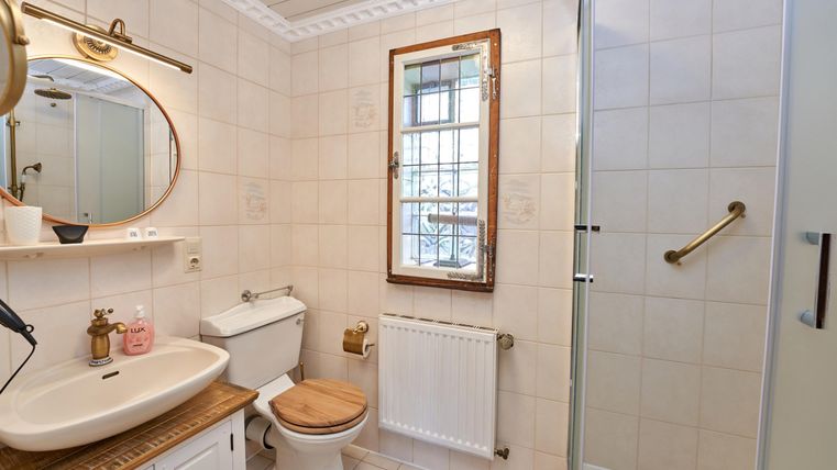 Ein helles Badezimmer mit einer Dusche, Waschbecken und Toilette. Die Wände sind gefliest, und ein runder Spiegel hängt über dem Waschbecken.